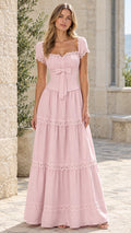 Full-length front view of woman wearing blush pink tiered lace maxi dress in a stone courtyard