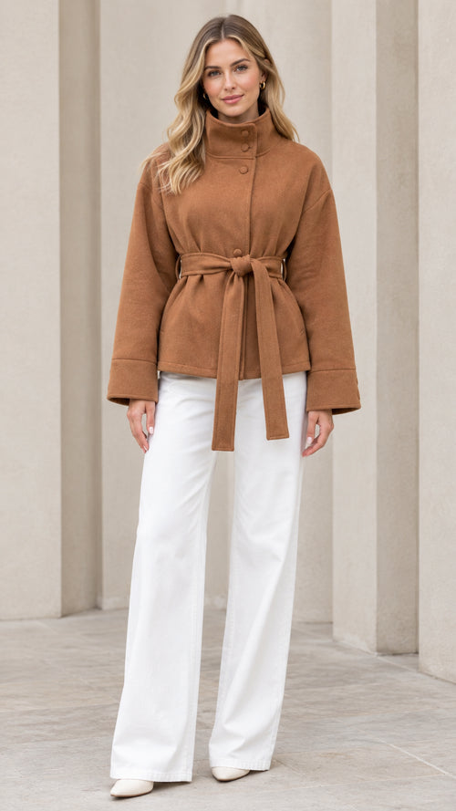 Front view of model wearing camel stand collar belted short coat with white trousers