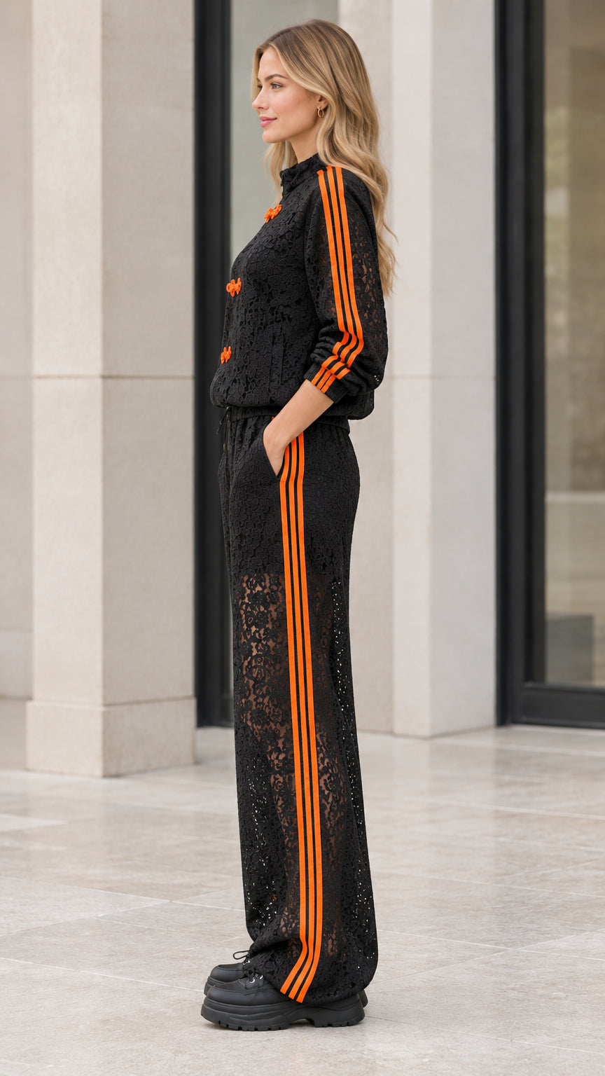 Side profile view of woman wearing black lace tracksuit with orange sleeve and pant stripes