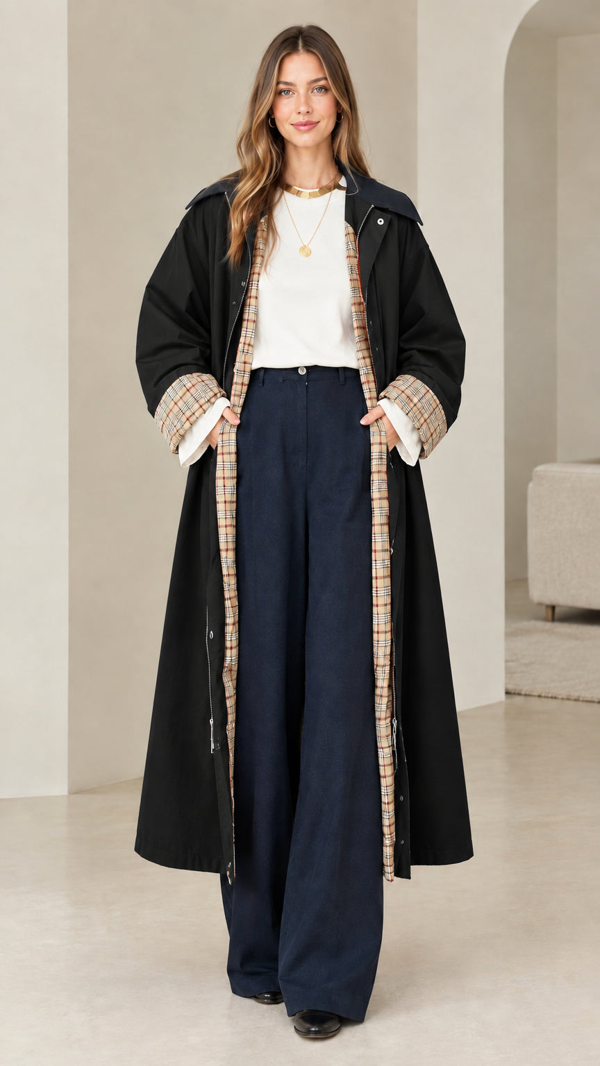 Front view of model wearing black longline trench coat with plaid cuff accents